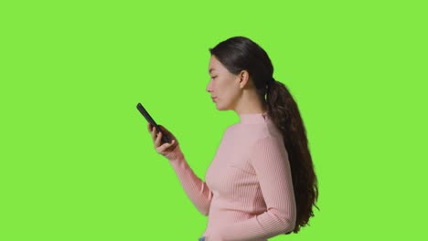 Profile-Studio-Shot-Of-Woman-Using-Mobile-Phone-Against-Green-Screen